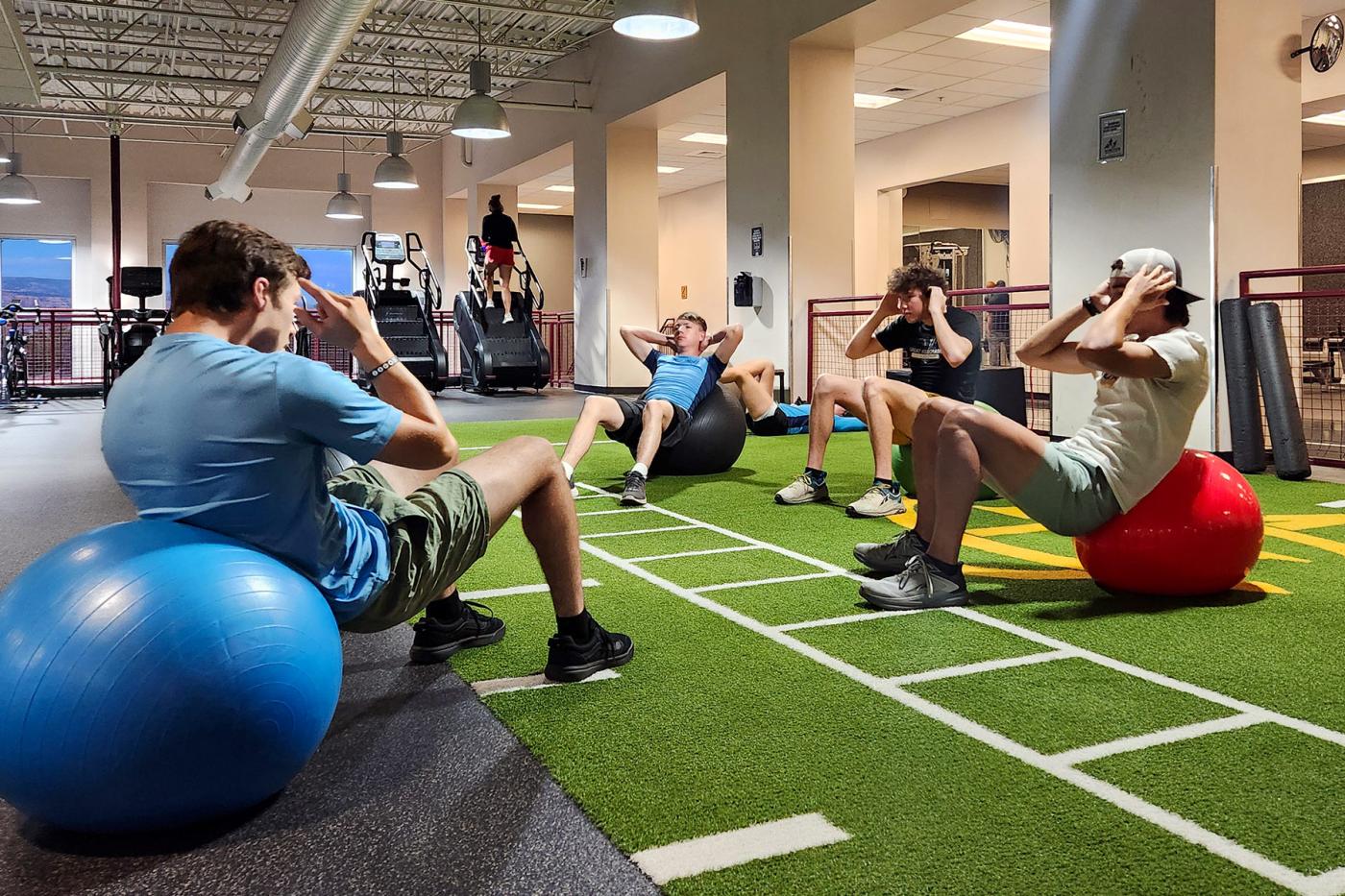 College athletes doing core exercises on stability balls inside a gym during dryland training.